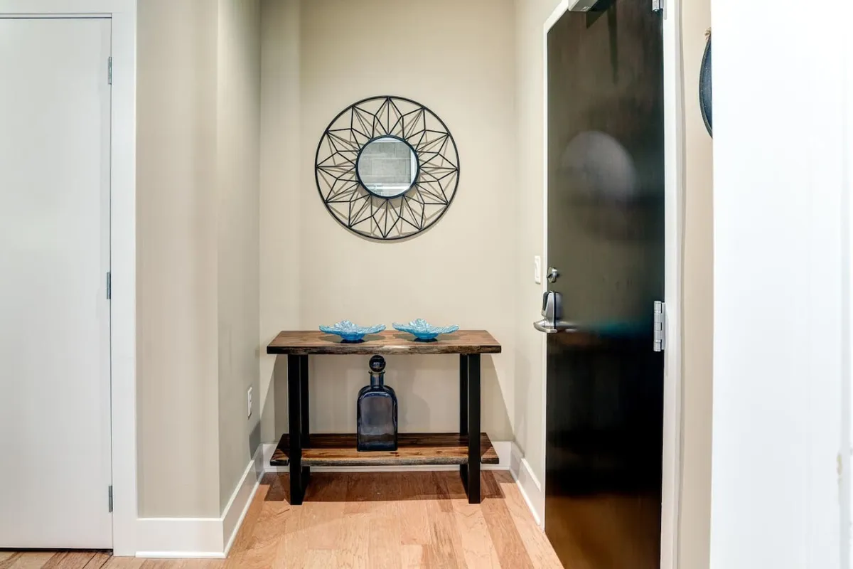 A wooden entry table topped with blue decorative bowls sits beneath a decorative mirror near a black entrance door. The space is inviting and sets a welcoming tone as soon as guests step inside from the city.