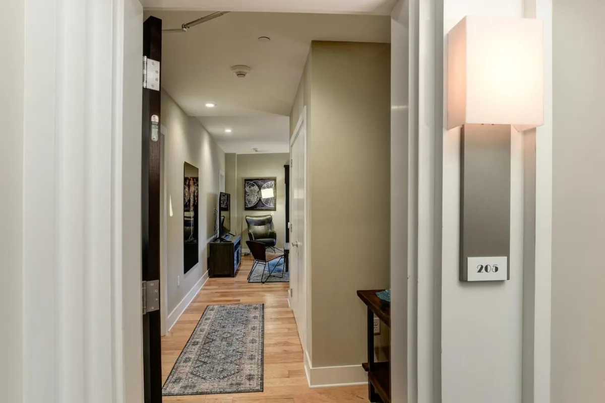 A cozy hallway leads to the living area, featuring a rug, chair, and television. The mood is inviting, hinting at a relaxed environment perfect for unwinding after a day in the city.