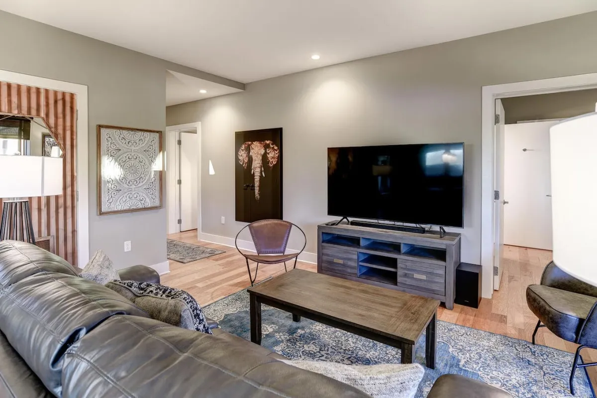 A modern living room with comfortable sofa, contemporary artwork, a stylish lamp, and a large television. The decor is sleek yet inviting, emphasizing both relaxation and opportunities for entertainment.
