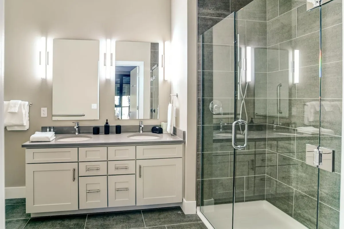 A bright, spacious ensuite bathroom boasting a double vanity with modern sinks, large mirrors, stylish lighting, and a walk-in shower. The design is both functional and tranquil, ideal for self-care and morning routines.