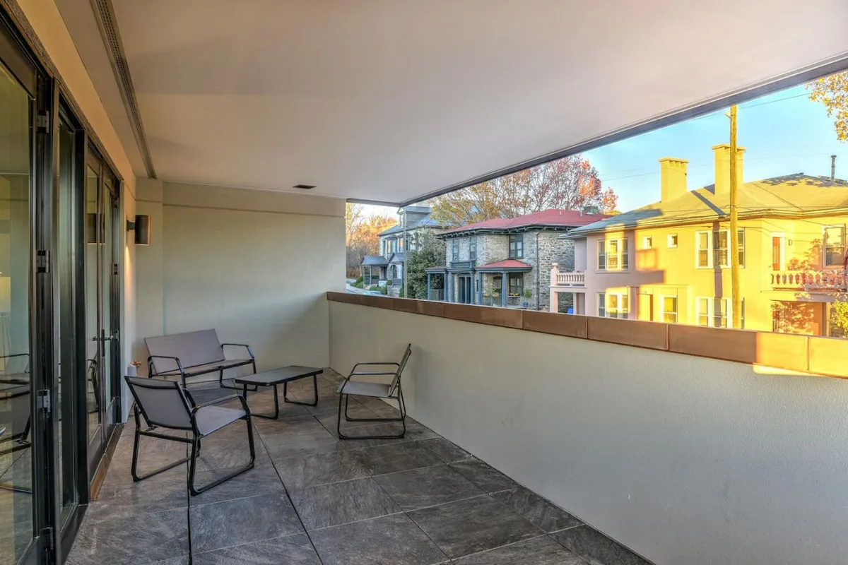 An outdoor seating area is set against sliding glass doors, with a view of neighboring houses. The relaxed setting includes comfortable chairs and a small table, making it perfect for reading, sipping coffee, or entertaining guests while enjoying fresh air and the urban backdrop.