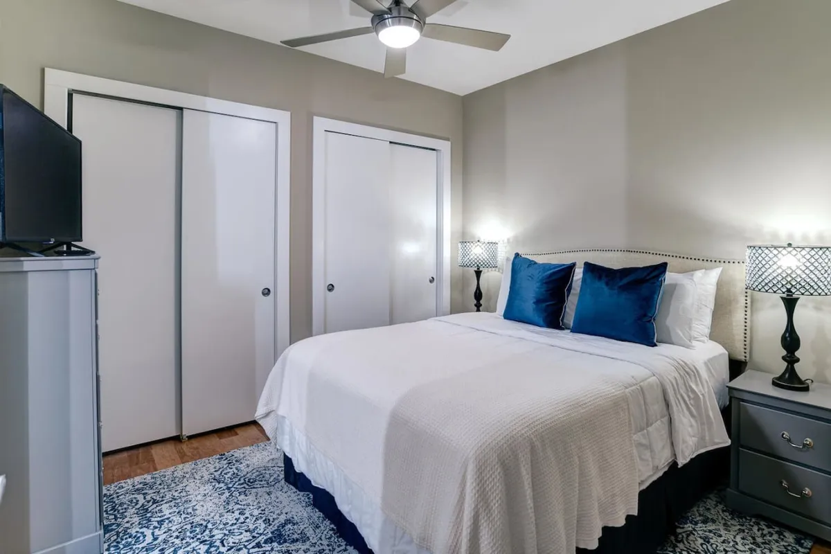 A well-appointed master bedroom with a large bed dressed in decorative pillows, two nightstands with elegant lamps, and a cozy area rug. The room exudes a calming, restful vibe—perfect for winding down after a day in the city.